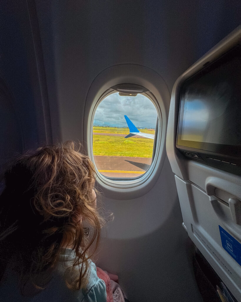 Child gazing out the airplane window as it lands in Kauai, showcasing a trip booked with a combination of flexible and fixed points for budget-friendly travel. Photo by Amy Berrian.